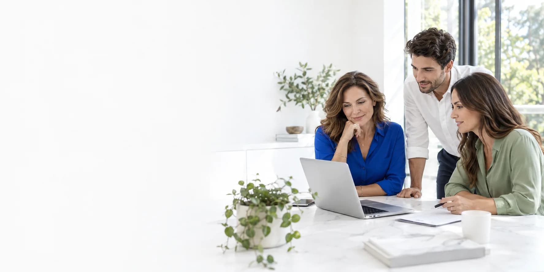 A business owner and two colleagues reviewing their work together at a laptop in a bright office